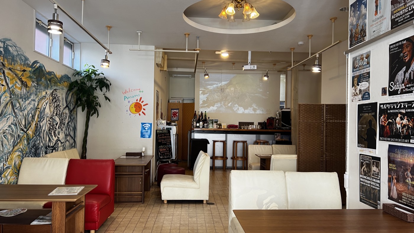 店内全景。左の壁に奄美の大きな壁画、奥にカウンターとプロジェクターの映像